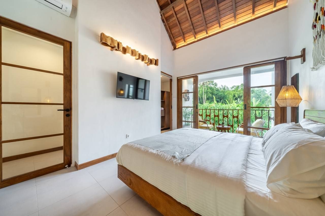 Bedroom with exposed beams, full-height doors to the balcony and a view of the greenery